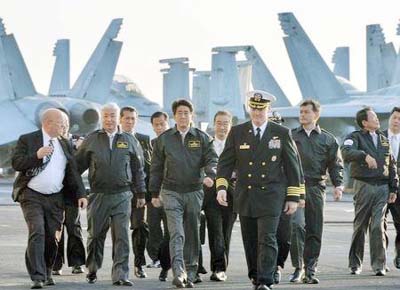 Japan's Prime Minister Shinzo Abe (C), Deputy Prime Minister and Finance Minister Taro Aso (2nd R) and Defence Minister Gen Nakatani (2nd L) walk with Chris Bolt, the captain of the USS Ronald Reagan, a Nimitz-class nuclear-powered super carrier, as they