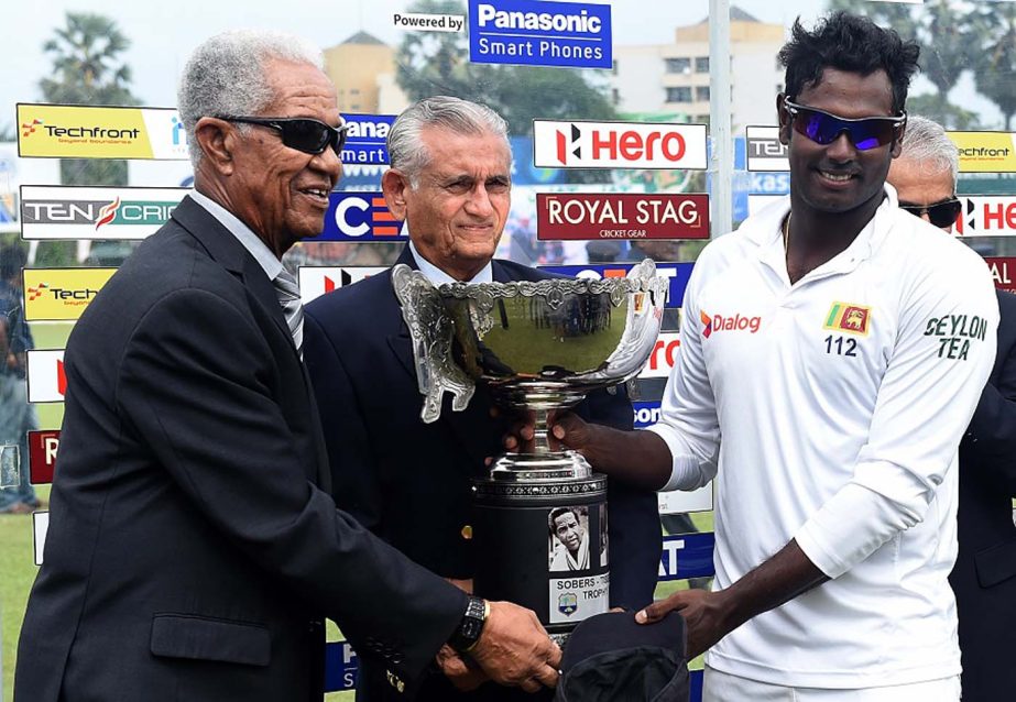 Sri Lankan cricket captain Angelo Mathews (R) West Indian cricket legend Garfield Sobers (L) and former Sri Lanka cricket captain Michael Tissera (C) hold up the Sobers/Tissera Trophy after Sri Lanka's victory in the Test match series between Sri Lanka a