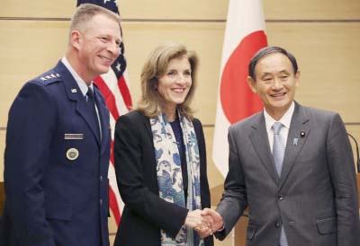 Japanese Chief Cabinet Secretary Yoshihide Suga, right, shakes hands with U.S. Ambassador to Japan Caroline Kennedy, centre, as Lt. Gen. John Dolan, Commander of U.S. Forces Japan, smiles after their joint press conference at Japanese Prime Minister's of