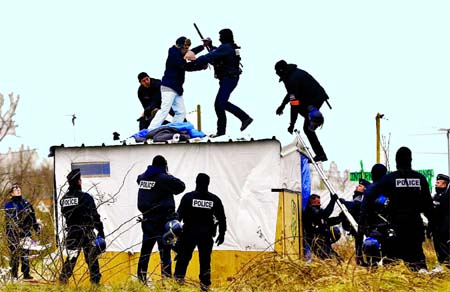 A group of anti-riot police officers apprehend a man protesting his eviction from the 'Jungle' on top of a dwelling inside the campsite. Internet photo