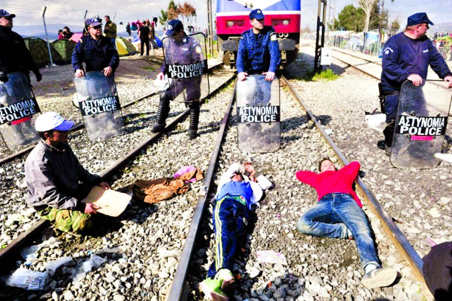 People sit and lie on train tracks in front of Greek policemen during a protest of migrants and refugees to call for the opening of the borders, blocking a train coming from Macedonia in a makeshift camp at the Greek-Macedonian border.