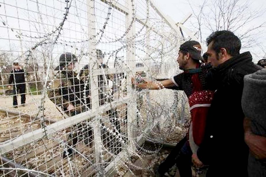 Refugees and migrants stand next to a border fence at the Greek-Macedonian border, after Macedonia closed its borders with Greece for Afghan migrants.