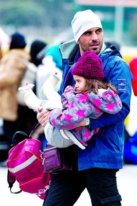 A Syrian man carries a child as migrants and refugees who just arrived with a ferry from Greek island prepare to get on busses with destination a transit camp at the port of Piraeus near Athen. Internet photo