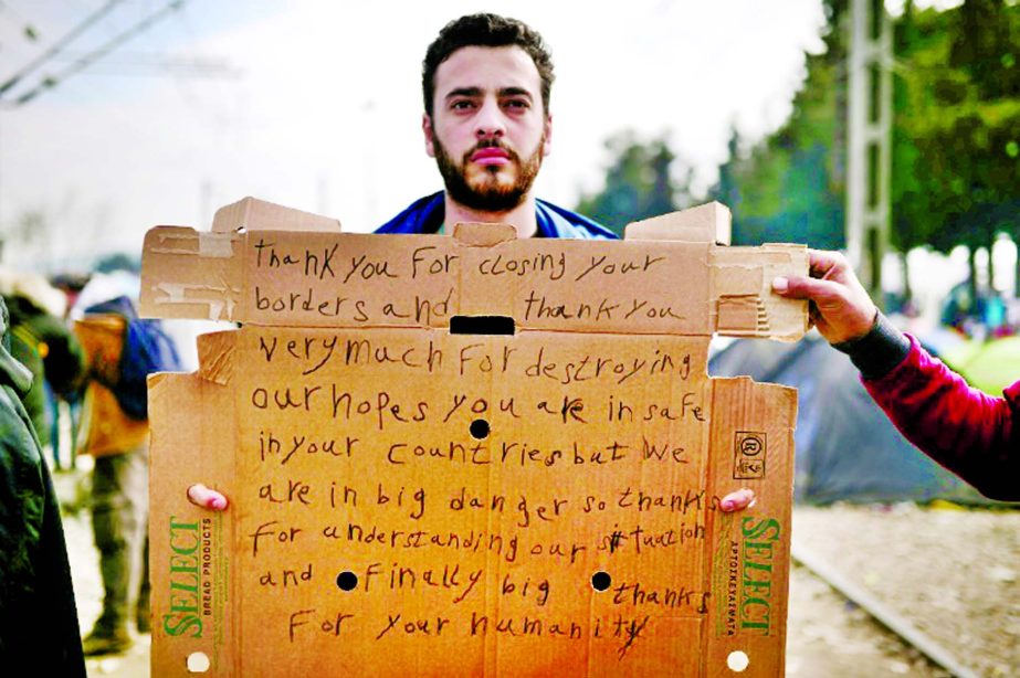 A man holds a sign in the makeshift camp at the Greek-Macedonian border, near the village of Idomeni, where thousands of refugees and migrants are stranded.
