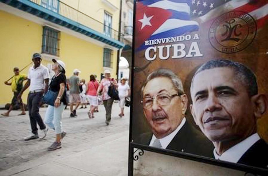 Tourists pass by images of U.S. President Barack Obama and Cuban President Raul Castro in a banner that reads "Welcome to Cuba"" at the entrance of a restaurant in downtown Havana."