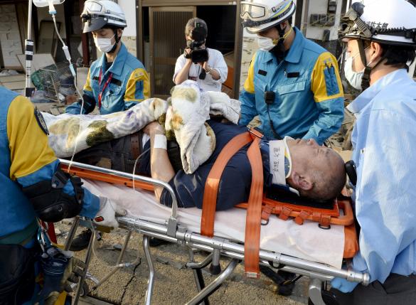 A man is carried away by a rescue workers after being rescued from his collapsed home caused by an earthquake in Mashiki town, Kumamoto prefecture, southern Japan, in this photo taken by Kyodo April 16, 2016. Mandatory credit ReutersKyodo