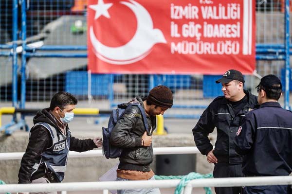 Police escort a migrant from a Turkish ferry carrying a group deported from Europe to Turkey in the Port of Dikili district in Izmir.