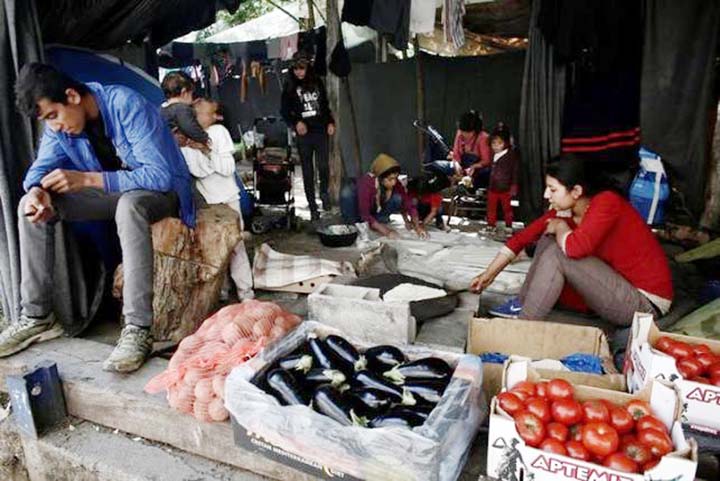 A refugee sits by his grocery stall as women cook traditional Arabic bread at a camp for refugees and migrants at the Greek-Macedonian border near the village of Idomeni.