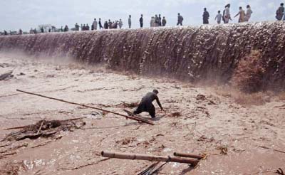 A shopkeeper tries to save belongings as residents use a bridge covered with floodwater after heavy rain in Nowshera District on the outskirts of Peshawar..