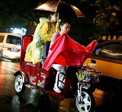 A woman and a girl ride on an electric bike on a rainy night in Beijing..