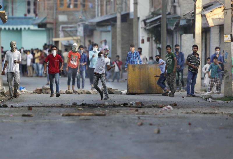 A Kashmiri protester throws a stone at Indian policemen during a protest in Srinagar, Indian controlled Kashmir, Monday.