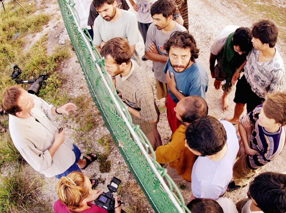 Refugees, right, gather on one side of a fence to talk with international journalists about their journey that brought them to the Island of Nauru.