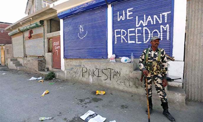 An Indian policeman stands guard near shops painted with graffiti during curfew in Srinagar on Friday.