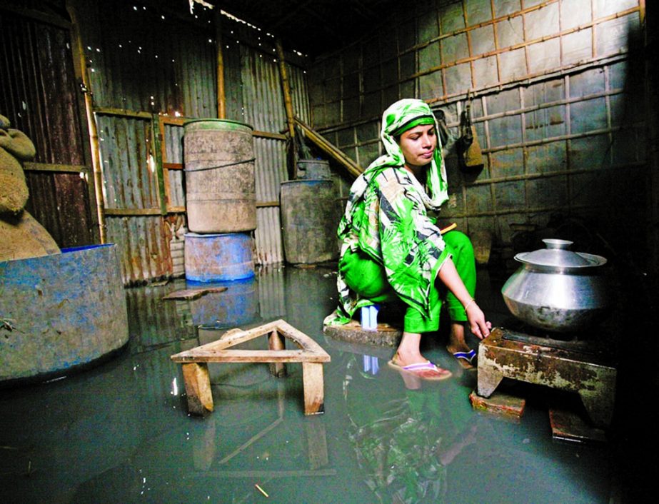 A woman cooking food in appalling situation as flood waters entered the kitchen room in Kamrangir Char area in the city on Saturday.