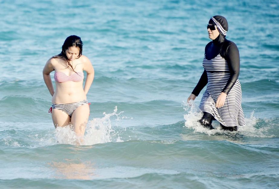 Tunisian women, one (right) wearing a "burkini", a full-body swimsuit designed for Muslim women, swim near Bizerte, north-east of the capital Tunis.