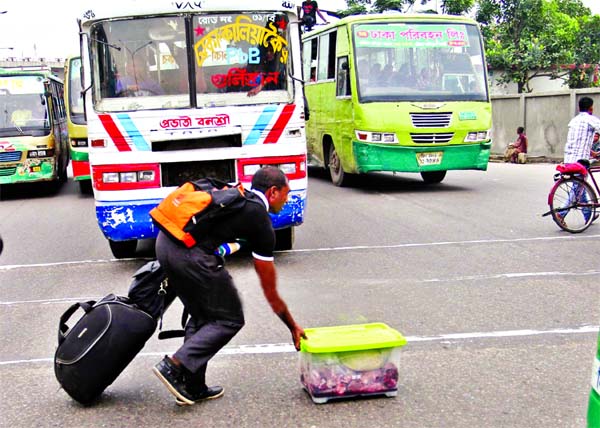 HERO INDEED! Desperate bid by a youth to cross the road with all his bag and luggage risking life when busy heavy passenger buses are plying there. This photo was taken on Biswa Road area on Tuesday.