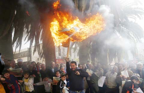 A Palestinian protester burns an Israeli flag during a rally gathering Muslims, Christians and Samaritans to protest against an Israeli draft bill that would limit the volume of calls to prayer at mosques in Israel and Jerusalem, Nablus.