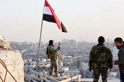 A Syrian government soldier gestures a v-sign under the Syrian national flag near a general view of eastern Aleppo after they took control of al-Sakhour neigbourhood in Aleppo, Syria