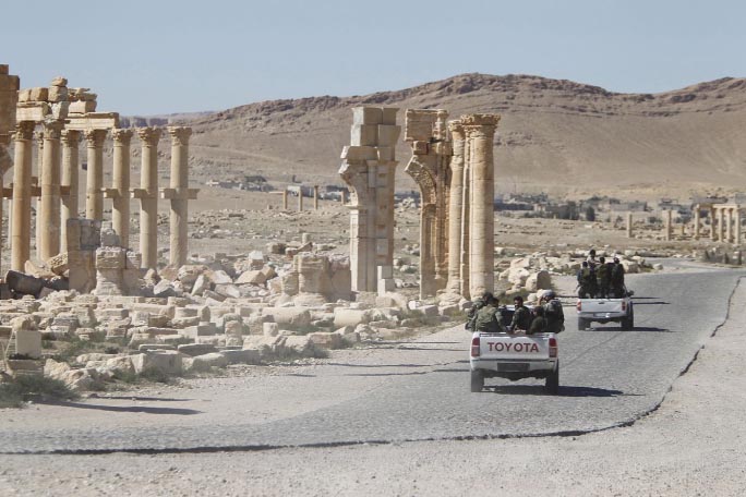 Syrian army soldiers drive past the Arch of Triumph in the historic city of Palmyra, in Homs Governorate.