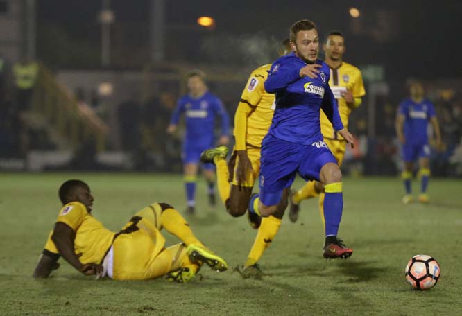 AFC Wimbledon's Dean Parrett escapes the tackle of Sutton United's Kevin Amankwaah during the English FA Cup third round replay soccer match between AFC Wimbledon against Sutton United at Cherry Red Record Stadium in south west London on Tuesday.