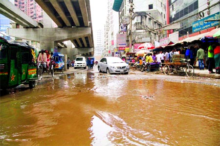 Vast area of potholes waterlogged including muddy and concrete rubbish due to blockade of drains causing sufferings to commuters and movement of vehicles. This photo was taken from near Mouchak Market under-construction flyover on Thursday.