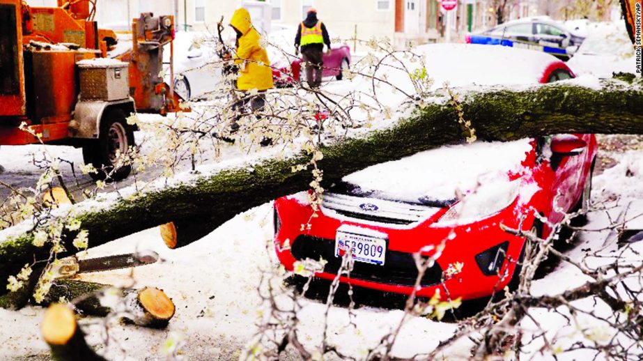 Workers clear debris after a tree branch fell on parked car in Baltimore on 15 March.