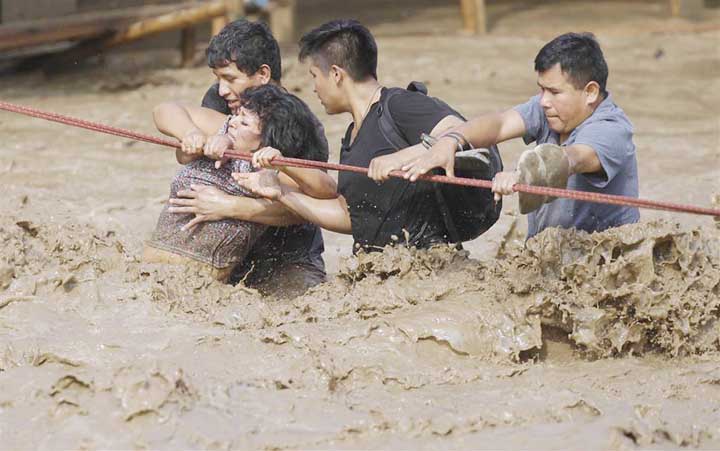 A group of people, stranded in flood waters, hold onto a rope as they wade through flood waters to safety in Lima, Peru.