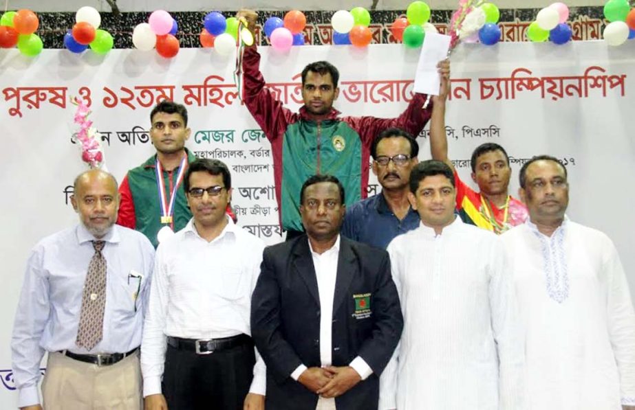 Ainuddin of Bangladesh Ansar showing his gold medal after earning the medal in the 56 kg weight category of the ARK Group 35th National Weightlifting (Men's) Championship with the officials of Bangladesh Weightlifting Federation pose for photograph at th