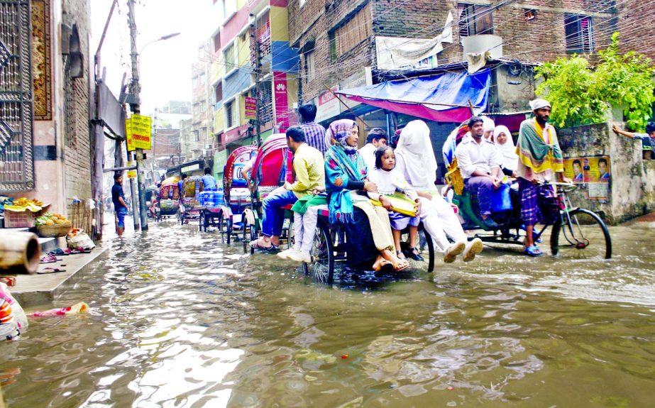 Rain water remains stagnant due to poor drainage system in different areas of the city, causing immense sufferings to commuters. Photo shows people including students passing the Nazimuddin Road with rickshaw-van pullers on Monday.
