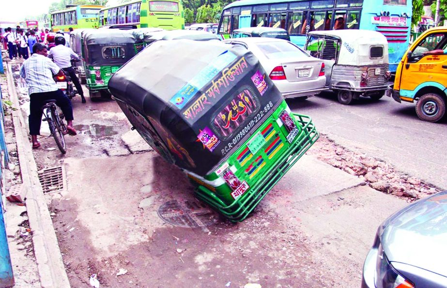 A three-wheeler CNG run vehicle being stuck at a pothole on the main road near Rafa Plaza in city's Dhanmondi area on Saturday as digging portion work on the road still continue.