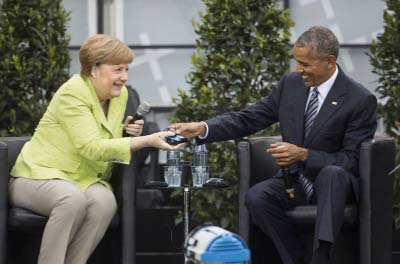 Former US President Barack Obama (right) and German Chancellor Angela Merkel smile as Obama hands over a headphone for translation during a discussion event on democracy and global responsibility at a Protestant conference in Berlin, Germany on Thursday,