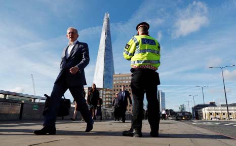 Commuters walk past a City of London police officer standing on London Bridge after is was reopened following an attack which left 7 people dead and dozens of injured in central London, Britain.