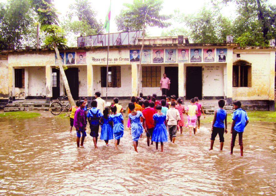 GANGACHARA (Rangpur): Students of Pirerhat Government Pry School in Gangachara Upazila entering into the school crossing knee-water as the school compound goes under water after normal rainfall. This snap was taken yesterday.