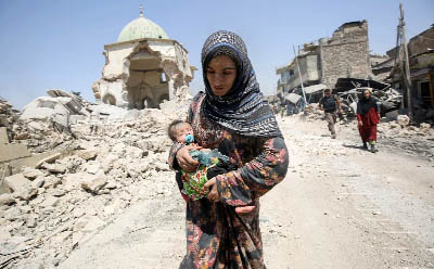 An Iraqi woman, carrying an infant, walks by the destroyed Al-Nuri Mosque as she flees from the Old City of Mosul .