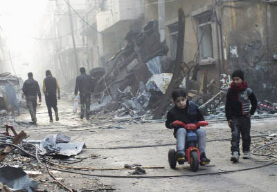 A boy rides on a tricycle along a damaged street in the besieged area of Homs, Syria.