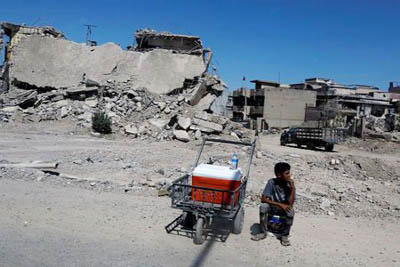 An Iraqi boy sells water in front of destroyed houses on a street in Western Mosul, Iraq.