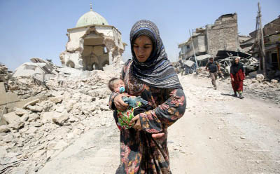 An Iraqi woman carrying a child walks by the destroyed Al-Nuri Mosque as she flees the Old City of Mosul.