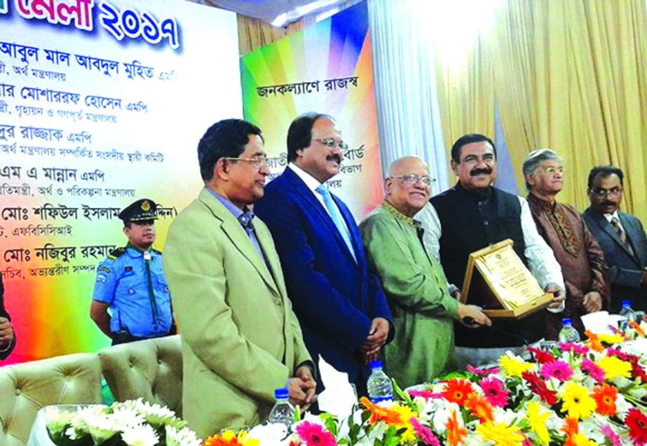 Finance Minister AMA Muhith, handing over the 'Kar Bahadur Paribar' award and 'Tax Card' to Shipping Minister Shajahan Khan and his family at the closing ceremony of weeklong Income Tax Fair at NBR's Agargaon office on Wednesday. State Minister for F