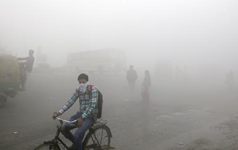 Indian commuters wait for transport amid thick blanket of smog on the outskirts of New Delhi, India on Friday