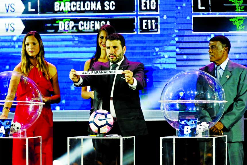 Conmebol Sports Secretary Hugo Figueredo holds up the name of Brazil's Atletico Paranaense during the Copa Sudamericana soccer tournament drawing ceremony in Luque, Paraguay on Wednesday. At left is Venezuela's star player Deyna Castellanos and at right
