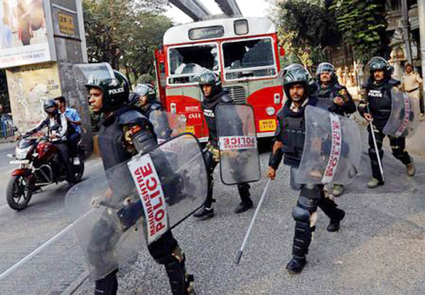 Riot police walk past a damaged public bus during a protest in Mumbai, India on Tuesday.