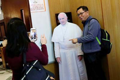 A Catholic poses for a photo with a cardboard cutout of Pope Francis at a church in Taipei, Taiwan