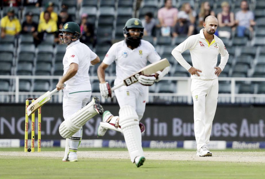 Australia's bowler Nathan Lyon (right) watches as South Africa's batsman Hashim Amla (centre) and teammate Dean Elgar, run between the wickets on day three of the fourth cricket Test match between South Africa and Australia at the Wanderers Stadium in J