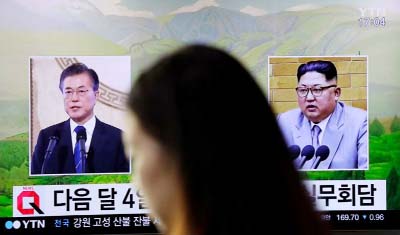 A visitor walks by a TV screen showing file footages of South Korean President Moon Jae-in, left, and North Korean leader Kim Jong Un, right, during a news program at the Seoul Railway Station in Seoul, South Korea