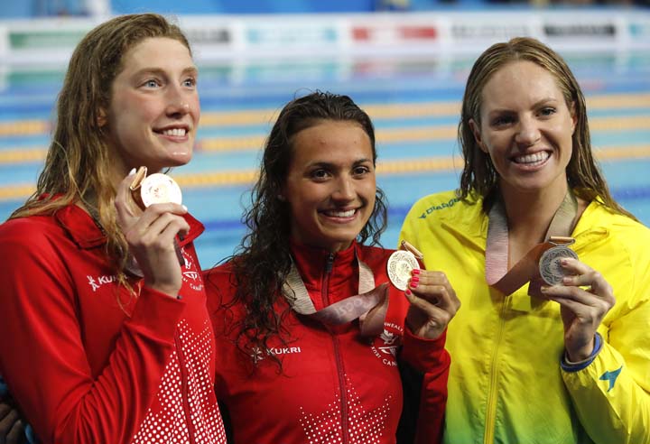 Women's 100m backstroke gold medalist Canada's Kylie Masse (centre) stands with silver medalist Australia's Emily Seebohm (right) and bronze medalist and compatriot Taylor Ruck at the Aquatic Centre during the 2018 Commonwealth Games on the Gold Coast,