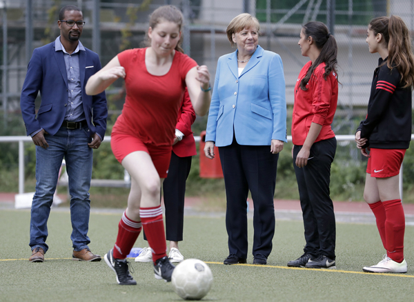 German Chancellor Angela Merkel (center) and the former German national soccer team player and integration commissioner of the German soccer association, Cacau (right) attend a women soccer training session at a soccer club in Berlin, Germany on Wednesday