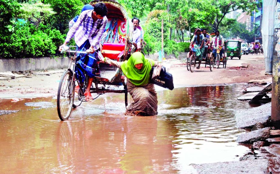 A woman fell into a ditch on a water logged road in the city as her rickshaw hit the pothole endangering her life. This photo has been taken on Wednesday from Rajarbagh area.