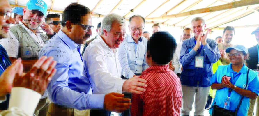 The United Nations Secretary-General AntÃ³nio Guterres (left), World Bank President Jim Yong Kim (center) and UNHCR High Commissioner Filippo Grandi (right) talking to a young Rohingya refugee in a camp.
