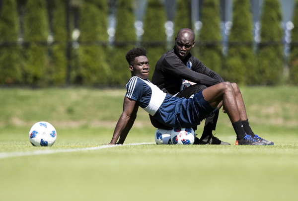Vancouver Whitecaps midfielder Alphonso Davies (front) sits with staff coach Pa-Modou Kah during practice in Vancouver on Monday.