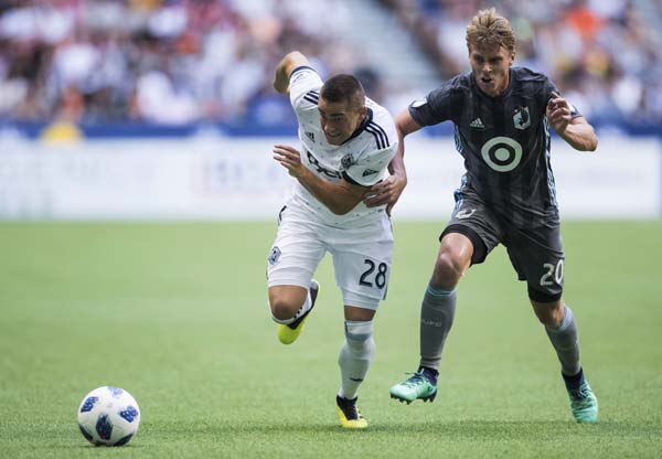 Vancouver Whitecaps' Jake Nerwinski (28) runs after the ball as Minnesota United's Rasmus Schuller (20) tries to hold him up during the first half of an MLS soccer match in Vancouver, British Columbia on Saturday.